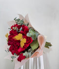 Ramo de 24 rosas rojas con follaje dólar y mariposas decorativas.