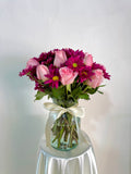Florero de cristal con rosas en tonos rosa y margaritas moradas
